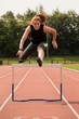 © Wavebreak Media - Female athletic running over hurdle on sports track
