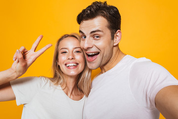 Loving couple standing isolated over yellow wall background take a selfie by camera.