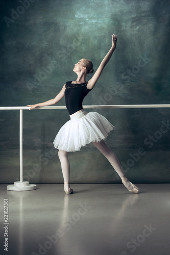 The classic ballet dancer in white tutu posing at ballet barre on studio  background. Young teen before dancing. Ballerina project with caucasian  model. The ballet, dance, art, contemporary - Buy this stock