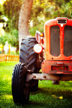 An Old Vintage Red Tractor Standing On A Farm Field At Sunset