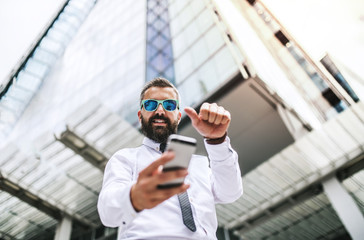 Wall Mural - Hipster businessman with smartphone standing on the street in London, taking selfie.