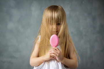 Wall Mural - little blonde girl with long hair combs her hair with a pink comb