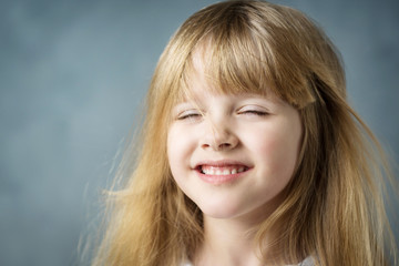 Wall Mural - smiling little blonde girl with fluttering hair with eyes closed