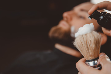 Wall Mural - Close-up razor in hands of barber, background client is waiting for shaving his beard and mustache.