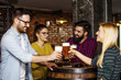© pucko_ns - Group of four people toasting with glasses full of beer in local pub