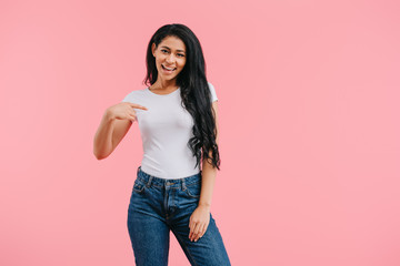 Wall Mural - portrait of smiling african american woman pointing at blank white shirt isolated on pink