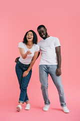 Wall Mural - laughing african american woman pointing at camera with boyfriend standing near on pink background