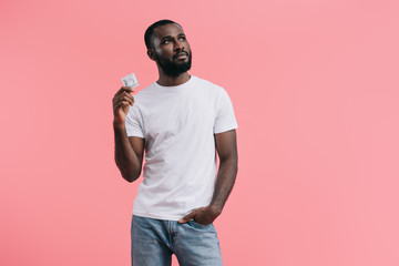 young african american man with condom looking away isolated on pink background