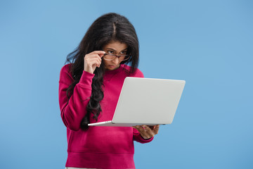 Wall Mural - focused young african american woman in eyeglasses looking at laptop isolated on blue background