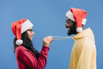 Sticker - side view of african american woman in christmas hat holding laces of boyfriend hoodie isolated on pink background