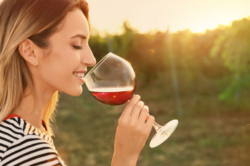 Wall Mural - Young beautiful woman enjoying wine at vineyard on sunny day. Space for text