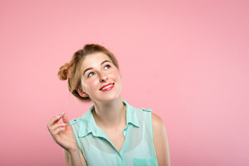 Wall Mural - smiling pretty young girl looking up and right at a virtual object or text speech bubble. empty space for advertising. portrait of a cute blond on pink background.