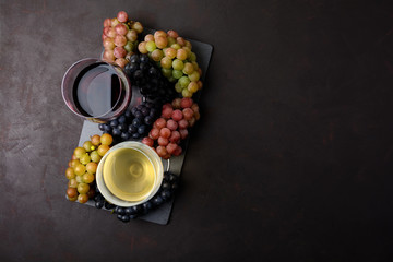 Wall Mural - Two wineglasses with red and white wine, bottles and grapes on dark wooden background. Top view. Flat lay. Copy space