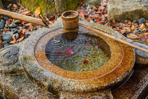 Fotografia, Obraz Old stone chozubachi for ritual ablution in Japan, with bamboo ladle and autumn