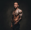 © Fxquadro - Portrait of a shirtless bearded tattooed male posing with hand in pocket. Isolated on dark textured background.