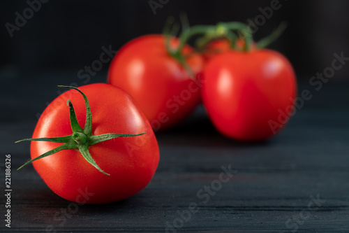 red tomatoes on a green branch on a black wooden background