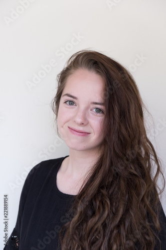 Fotografie, Obraz Cute brunette with long hair and black dress looking at camera and smiling, shoulders turned