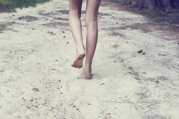 child girl bare feet walking along the forest sandy path.