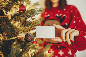 hand holding credit card close-up on background of golden beautiful christmas tree with lights in festive room. christmas shopping and sale concept. discount. black friday.