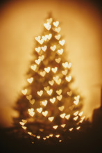 Beautiful Christmas Tree Golden Lights Hearts In Festive Room. Christmas Abstract Background, Blur Defocused Bokeh Of Yellow Glowing Hearts On Christmas Tree. Winter Holidays