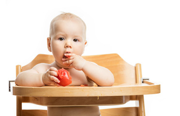 Wall Mural - Cute baby girl eating tomato while sitting in high chair over white