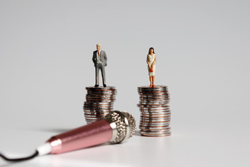 Wall Mural - Miniature man and miniature woman standing on a pile of coins of the same height with a pink microphone.