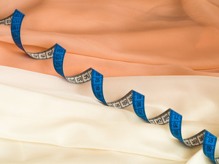 Close up of blue twisted tape measure on cream and beige fabric with undulation