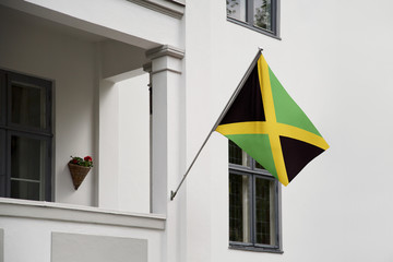 Wall Mural - Jamaica flag. Jamaica flag hanging on a pole in front of the house. National flag of waving on a home displaying on a pole on a front door of a building. Flag raised at a full staff.