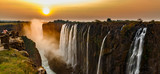 Fototapeta  - Victoria falls sunset panorama with orange sun and tourists