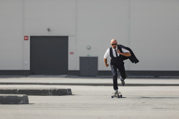 Confident young businessman in business suit on longboard hurrying to his office, on the street in the city
