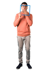 Full body of  Man in a pink sweatshirt looking through empty picture frame in front of face on isolated white background