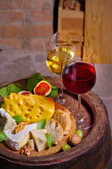 Red and white wine with cheese, grapes, figs and nuts on old cask in wine cellar. Glasses and bottles of wine