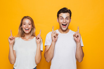 Wall Mural - Excited young loving couple standing isolated over yellow wall background pointing.