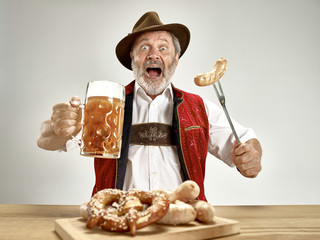 Germany, Bavaria, Upper Bavaria. The senior happy smiling man with beer dressed in traditional Austrian or Bavarian costume holding mug of beer at pub or studio. The celebration, oktoberfest, festival