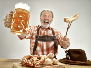 Germany, Bavaria, Upper Bavaria. The senior happy smiling man with beer dressed in traditional Austrian or Bavarian costume holding mug of beer at pub or studio. The celebration, oktoberfest, festival