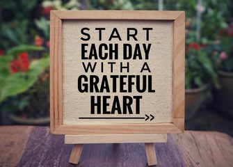 Motivational and inspirational quote - ‘Start each day with a grateful heart’ written on a framed white paper. Vintage styled background.