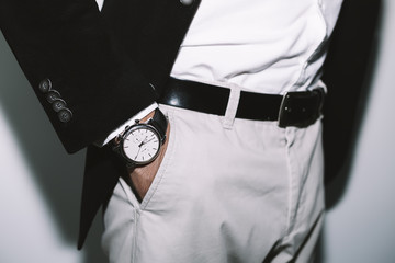 Wall Mural - Closeup fashion image of luxury watch on wrist of man.body detail of a business man.Man's hand in beige pants pocket closeup at white background.Man wearing black jacket and white shirt.Not isolated