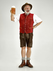 Wall Mural - Portrait of Oktoberfest senior man in hat, wearing a traditional Bavarian clothes standing with beer at full-length at studio. The celebration, oktoberfest, festival concept