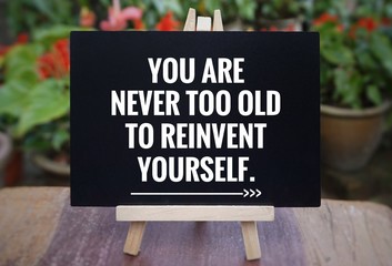 Wall Mural - Motivational and inspirational quote - ‘You are never too old to reinvent yourself’ written on a blackboard. Blurred vintage styled background.