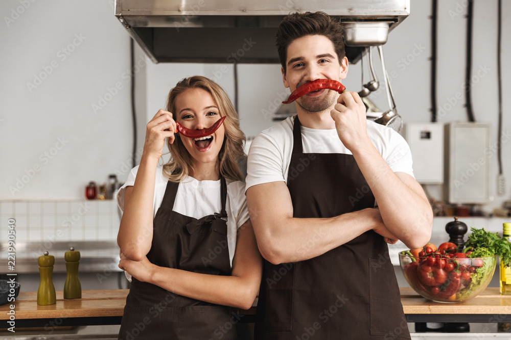 Friends loving couple chefs on the kitchen having fun with pepper as a moustache. - obrazy, fototapety, plakaty 