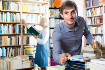 Wall Mural - Young glad man choosing new book from many