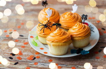 Wall Mural - food, baking and holidays concept - cupcakes or muffins with halloween party decorations and candies on plate