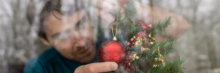 Young man hanging red Christmas decoration on a tree