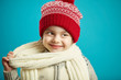 © Ilshat - Little girl in beautiful red hat and scarf stands on blue isolated background, close-up portrait