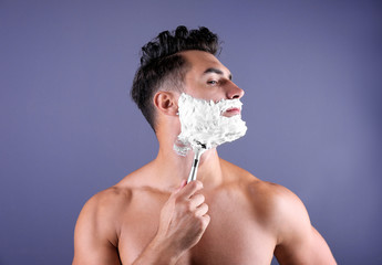 Handsome young man shaving on color background