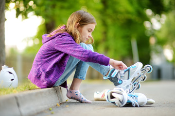 Wall Mural - Pretty little girl learning to roller skate on summer day in a park. Child wearing safety helmet enjoying roller skating ride outdoors.