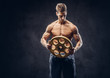 © Fxquadro - Handsome shirtless ectomorph bodybuilder with stylish hair posing with a barbell disk on dark background.