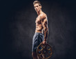 © Fxquadro - Handsome shirtless ectomorph bodybuilder with stylish hair posing with a barbell disk on dark background.