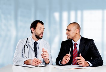 Wall Mural - Doctor smiling with  male patient at his desk in his office -