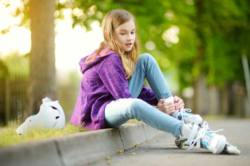 pretty little girl learning to roller skate on summer day in a park. child wearing safety helmet enj